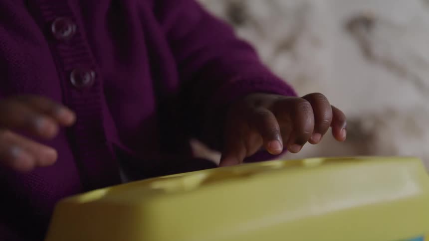 Baby places the yellow plastic lid on a block shape sorter toy at home