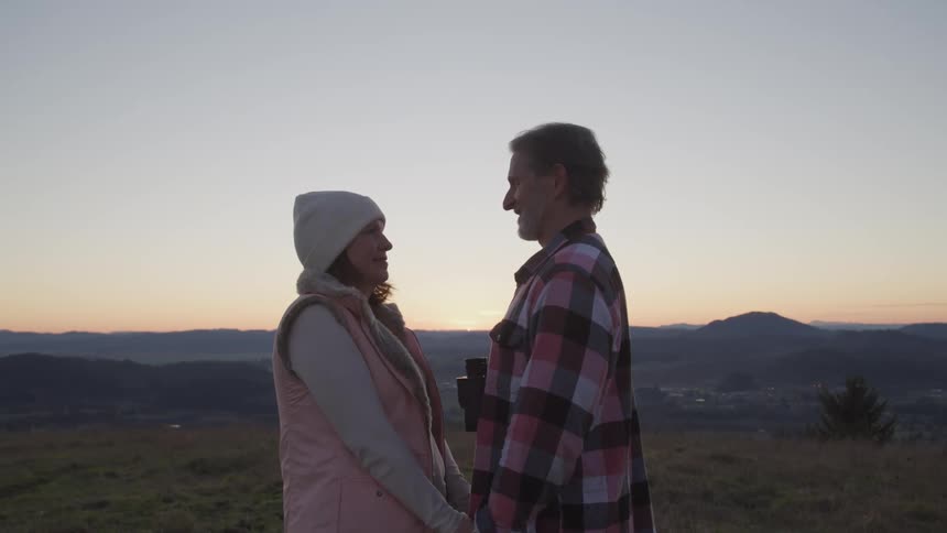 A man with a camera around his neck holds hands as he faces a woman and they stand in a field