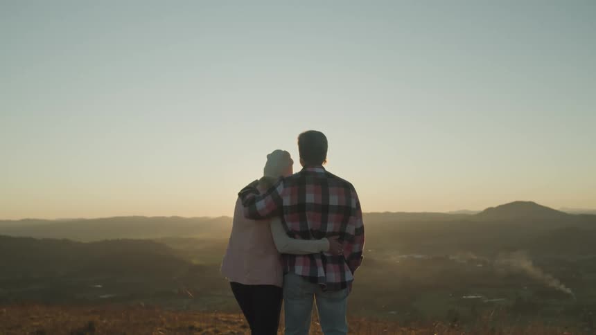 A man and a woman standing and hugging with the landscape and the sky in the background