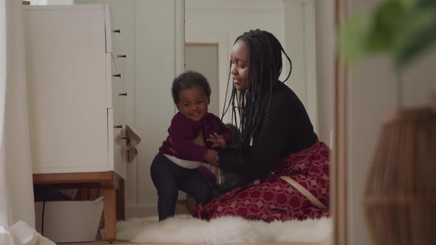 A woman kneels down to her small son trying to stand on the floor