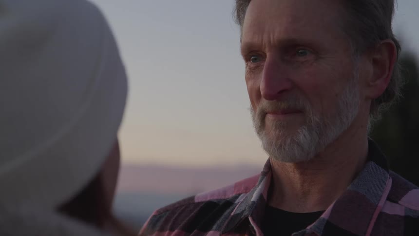 Bearded man standing outdoors at sunset looks a woman in the eyes