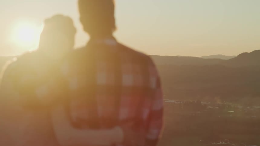 Couple holds each other and watches sunset on the hills