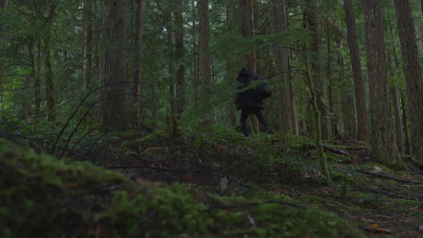 Man wearing a coat and a backpack runs uphill in the woods