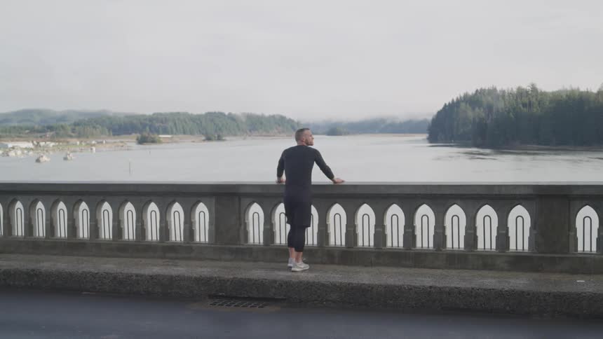 Man reclined on the railing of a bridge looks at the river