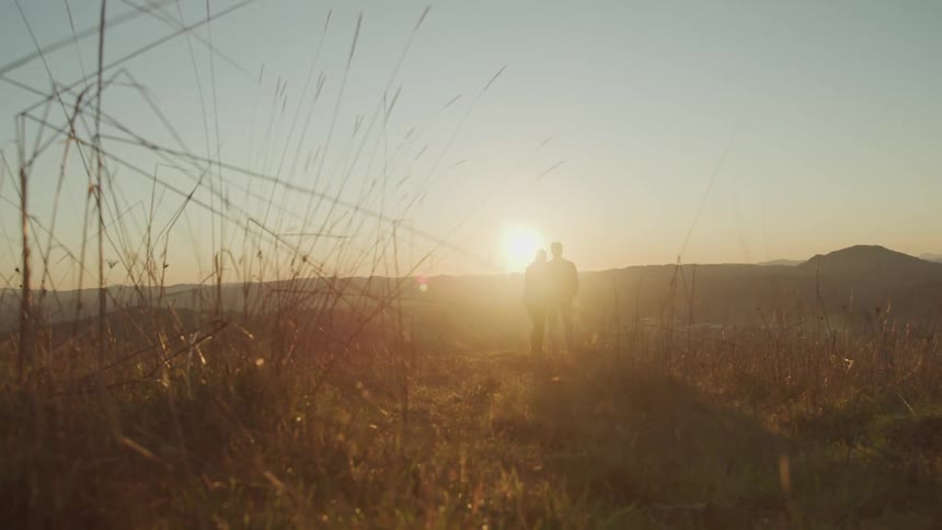 The low sun shines down on a pair of people standing in a grassland