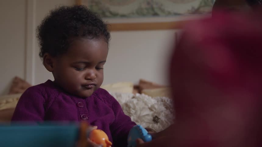 A baby holds a toy as her mother shows her another one and moves it through the air