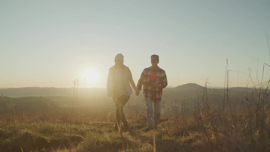 A man and woman hold hands walking through a rural field