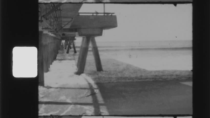 Person walks across beach toward area under pier