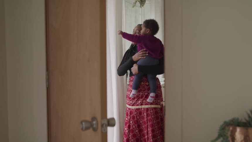 A woman holds a toddler boy and they look outside together