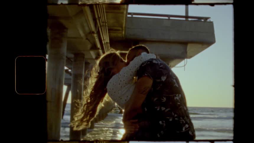 A man and woman hug and kiss under the pier by the ocean