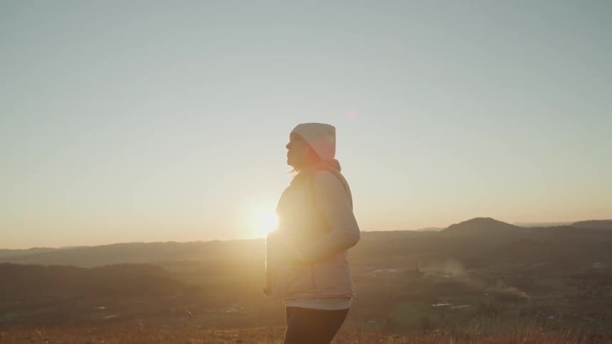 Woman stands on top of a hill at sunset