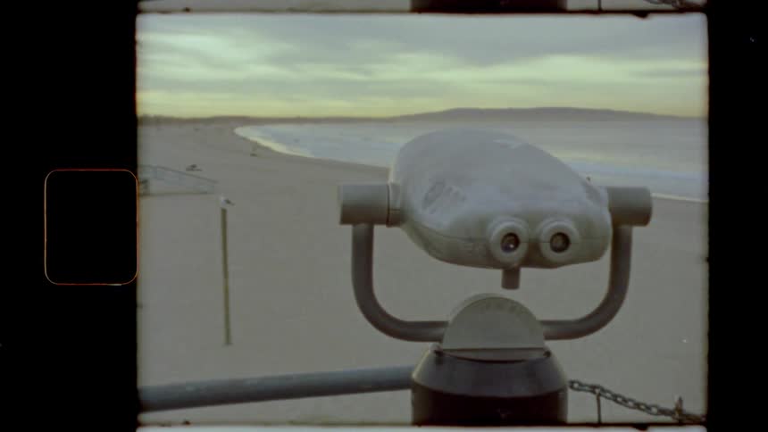 A boardwalk with binoculars with the beach the ocean and the sky in the background