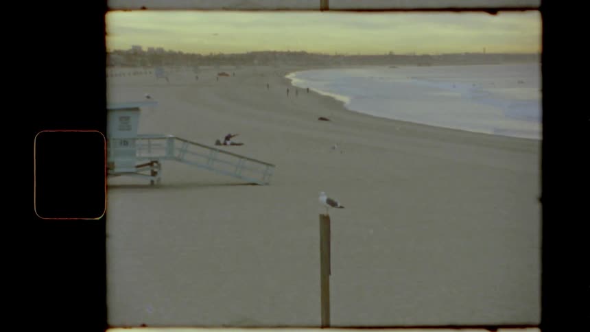 People walk and rest on a beach near a blue lifeguard station
