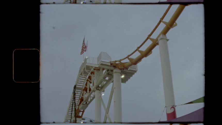A roller coaster track with flags waving in the wind and birds flying in the sky