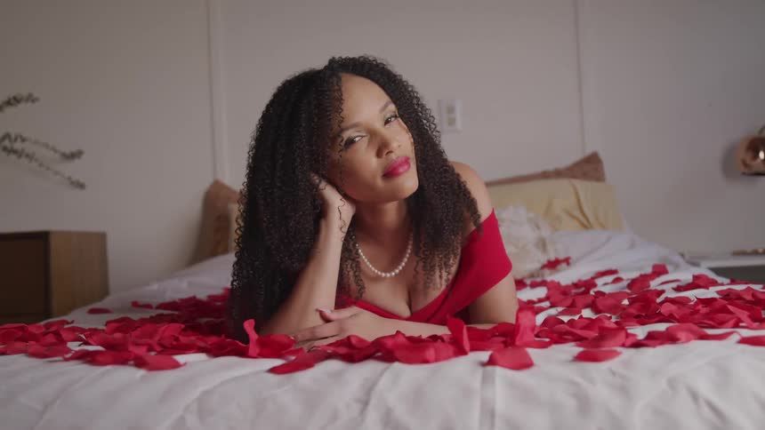 A woman lays on a bed covered with flower petals