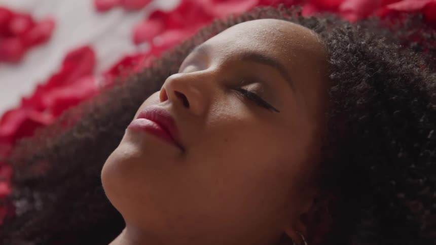 A woman with earrings and lipstick laying in a bed with flower petals