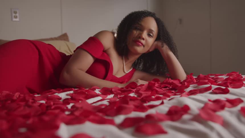 A woman is laying in the bed full of rose petals