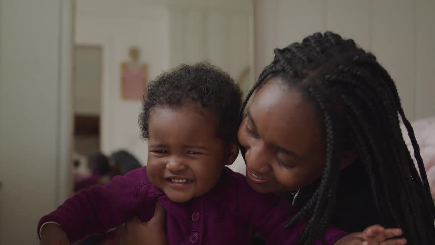 Black mother with braided hair holds her toddler boy and laugh together