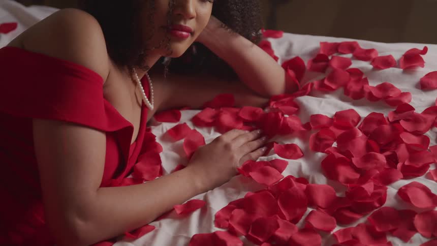 A woman lying on a bed with flower petals