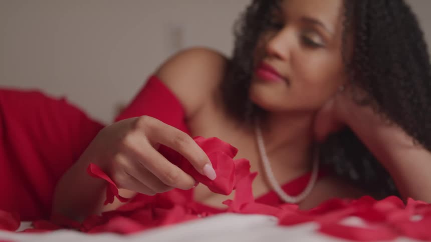 A woman is laying on the bed picking up rose petals