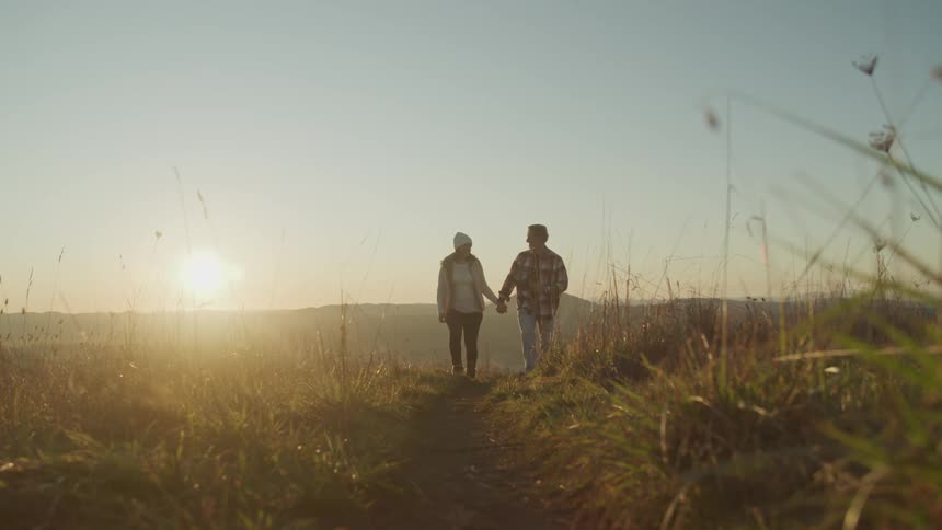 A man and woman hold hands walking through a field