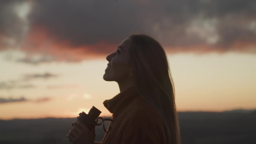 A woman holds binoculars as she looks up at the sky smiling as she stands in a canyon