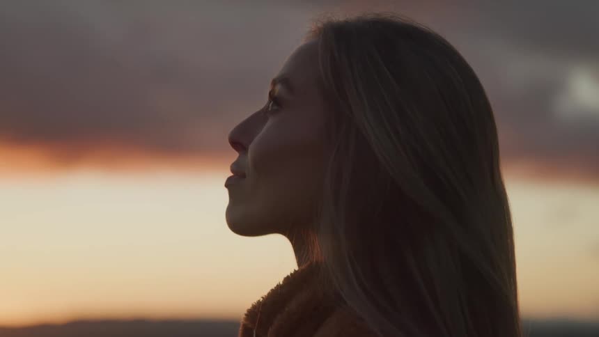 Side view of a woman with long brown hair looking up at the sky at sunset