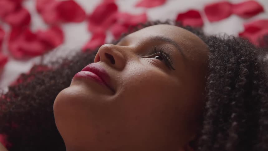 A woman laying down and looking up with flower petals in the background