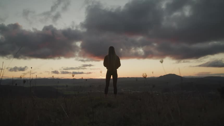 Woman with long hair and tights watching the horizon at sunset is silhouetted against the sky
