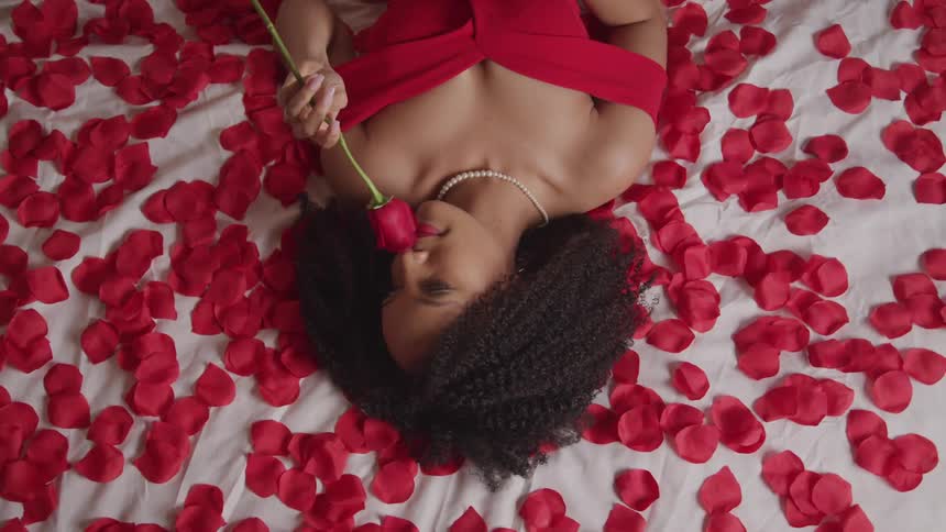 A young woman lies on a bed of rose petals and smells a single rose