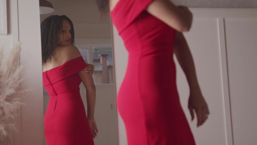A woman is looking at a mirror while wearing a dress