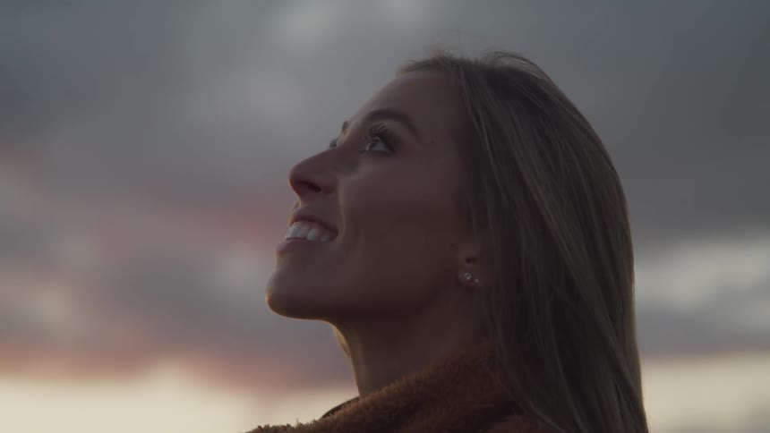 A woman standing outside smiles as she looks up at the sky