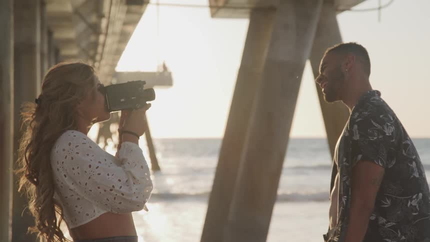 A woman is video recording a man on the beach