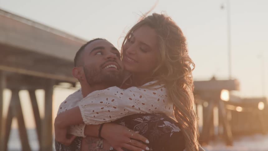 A young woman wraps her arms lovingly around her male companion as she kisses him