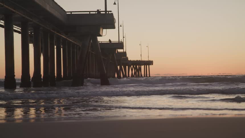 Ocean waves flowing beneath a pier at sunset