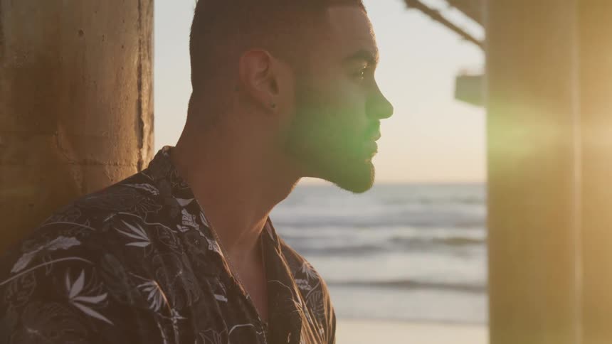 Young man under a wooden pier on the beach at sunset