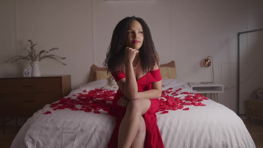 A woman is sitting on a bed with rose petals on it