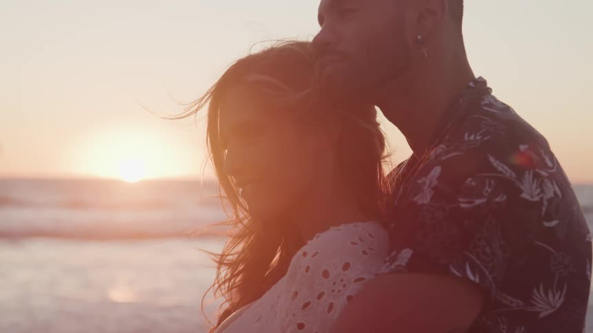 Man holds woman in his arms on beach at sunset
