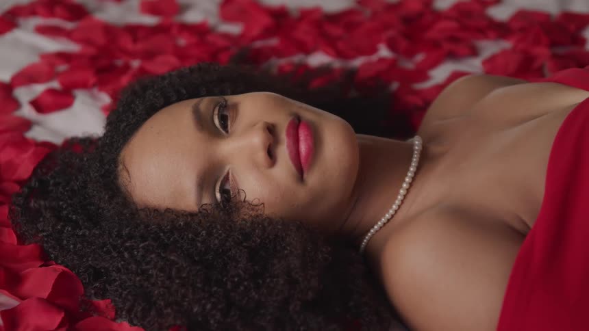 Black woman laying on a bed covered with rose petals