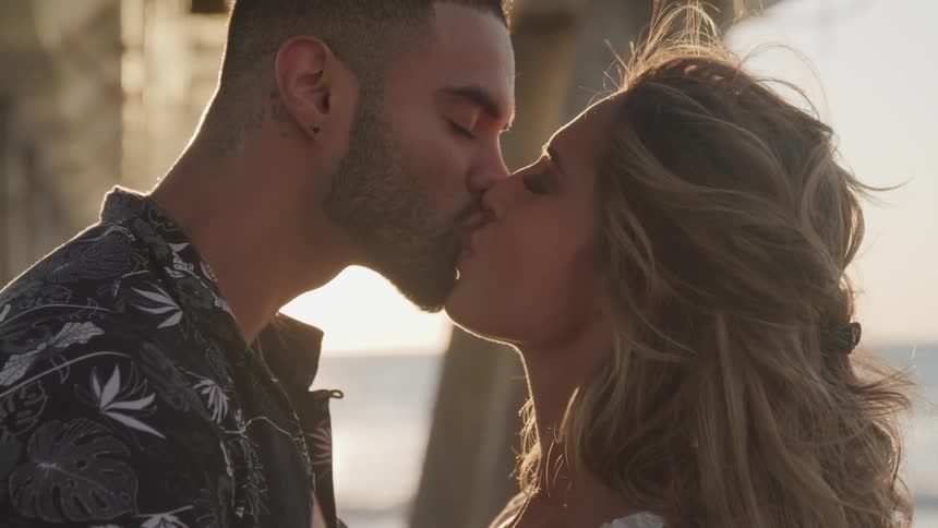 A man and woman kissing under a pier on the beach