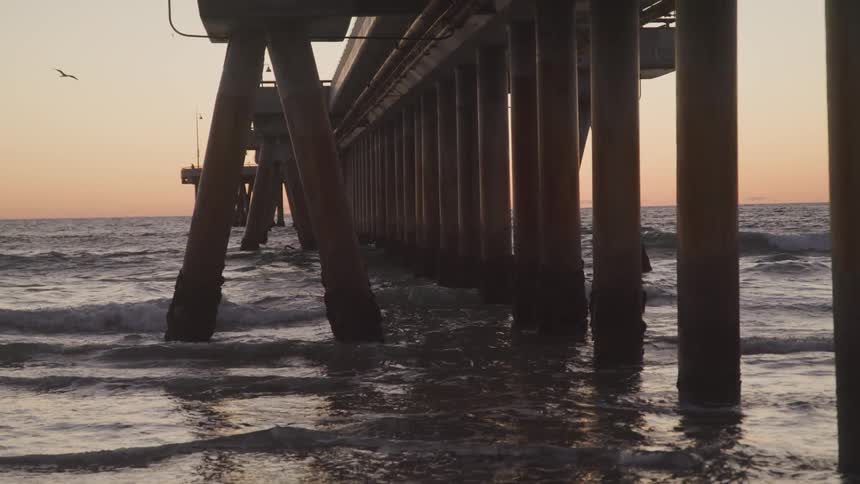 Ocean waves flowing beneath an ocean pier at sunset