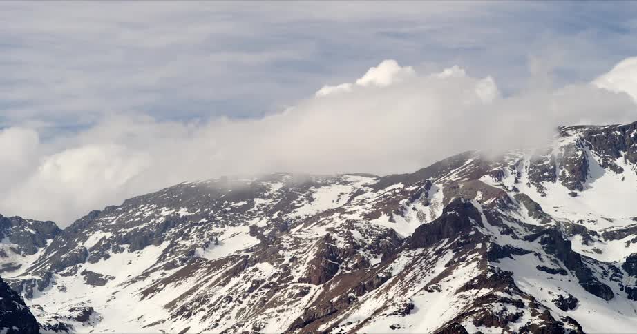 Time lapse of clouds rolling over the peaks of a snow covered mountain range