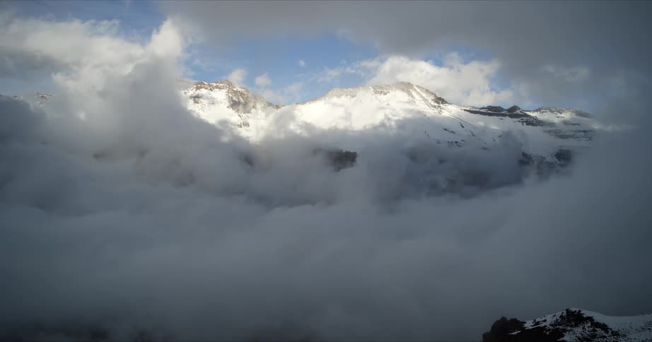 Clouds float around a snowy mountain range on a winter day