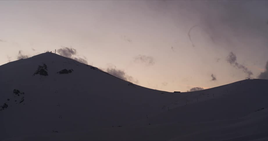 Wispy clouds move across a mountain at dusk