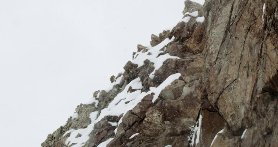 Snow gently falls from above and lands on a rocky mountain side