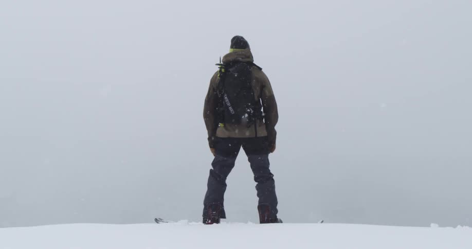 A snowboarder stands atop a mountain