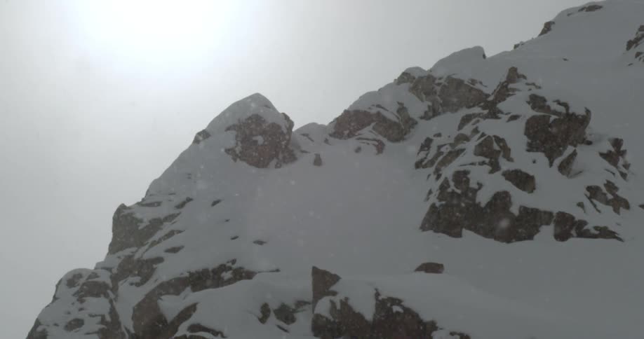 Snow falls around a mountain ridge on a winter day