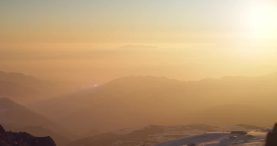 The sun shines down on a mountain range surrounded in fog