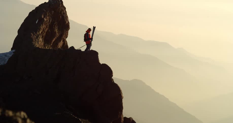 A person with skis on top of a mountain cliff