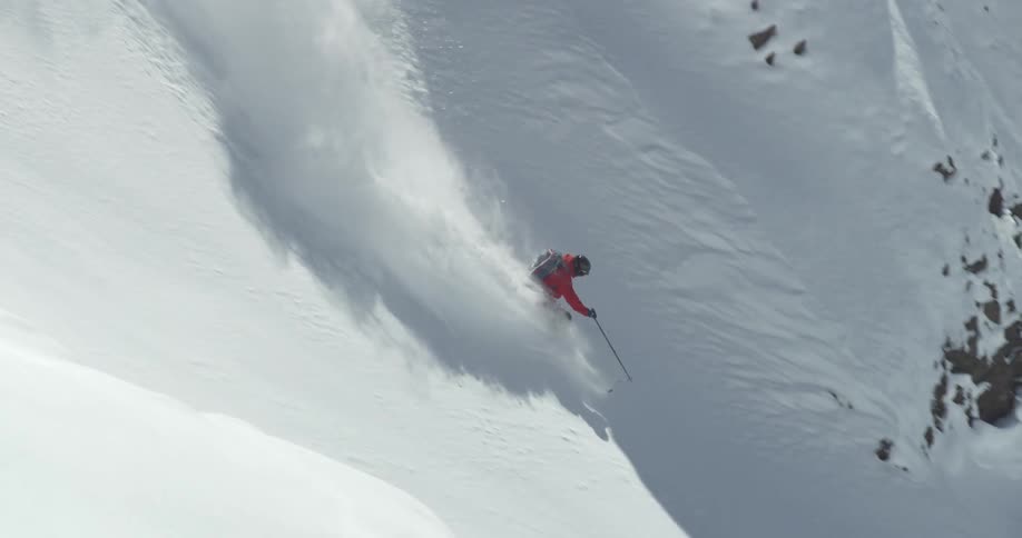 Skier skis down mountain slope kicking up snow in their wake
